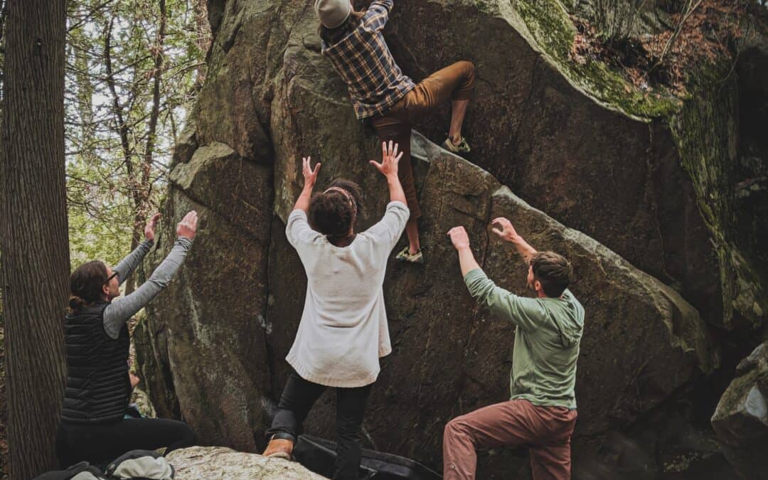 person climbing a rock with the help of friends